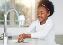 A child smiles as they wash their hands at the sink.