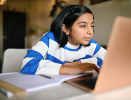 A child squints at her laptop as she does homework.