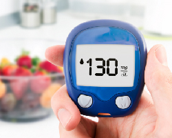 A hand holding a glucose monitor with a reading of 130.