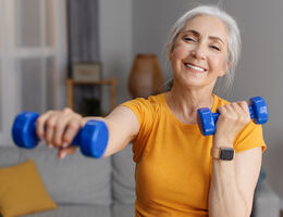 An older woman smiles as she uses a small pair of weights.