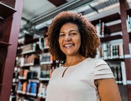 A smiling woman stands in front of library shelves.