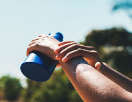 A person applying sunscreen to their arm outdoors.