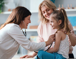 A doctor examines a smiling girl as a woman looks on.