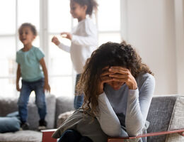 A mom with two kids sits in a chair with her head in her hands.