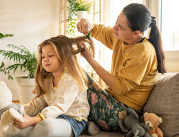 A woman brushes a girl’s hair with a fine-tooth comb.