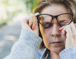 A woman lifts her glasses to rub her eye.