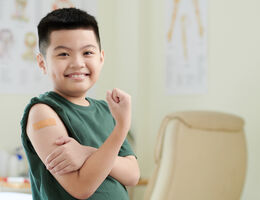 A child flexes a bare arm to display an adhesive bandage on their biceps.